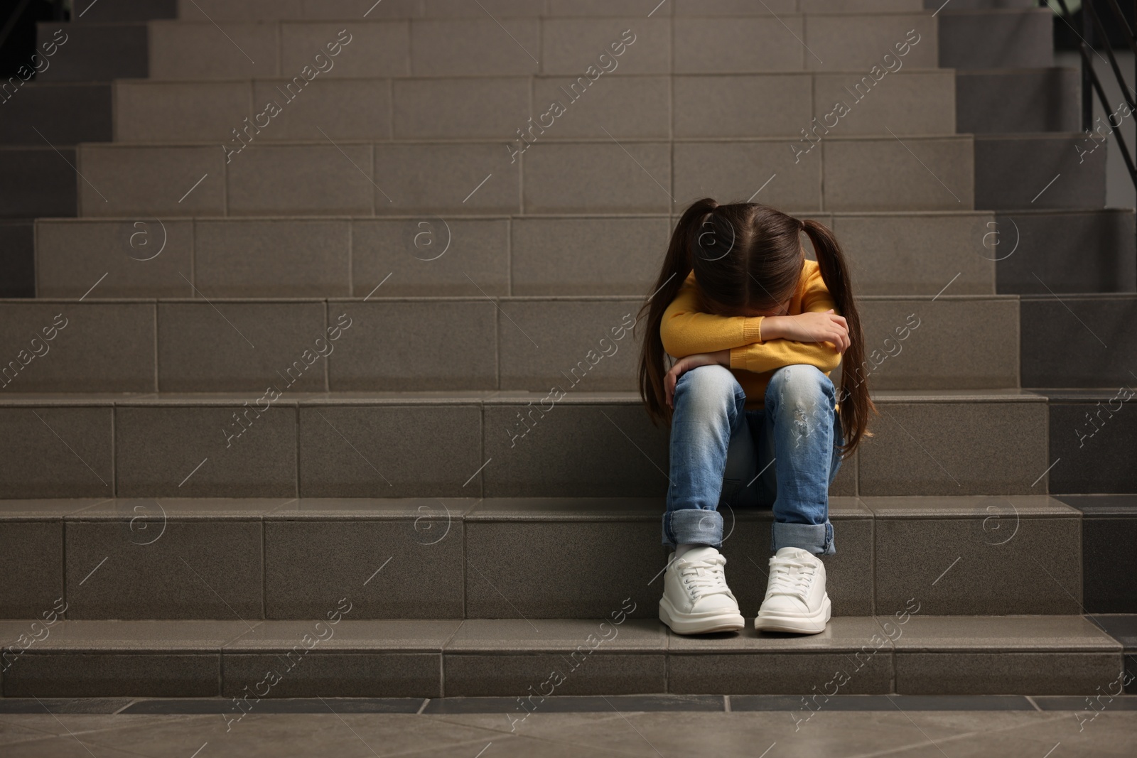 Photo of Child abuse. Upset little girl sitting on stairs, space for text