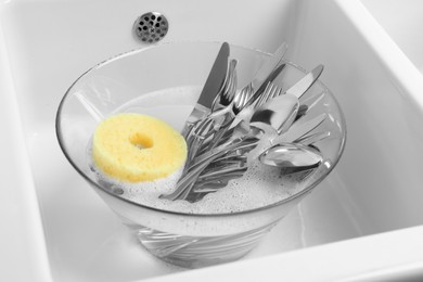 Photo of Washing silver spoons, forks and knives in kitchen sink