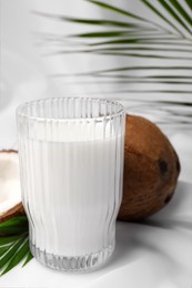 Photo of Glass of delicious coconut milk, palm leaves and coconuts on white table