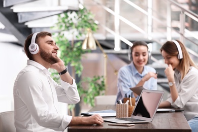 Photo of Young businessman with headphones, laptop and his colleagues at table in office