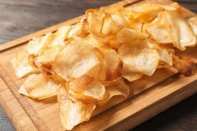 Photo of Wooden board with crispy potato chips on table, closeup