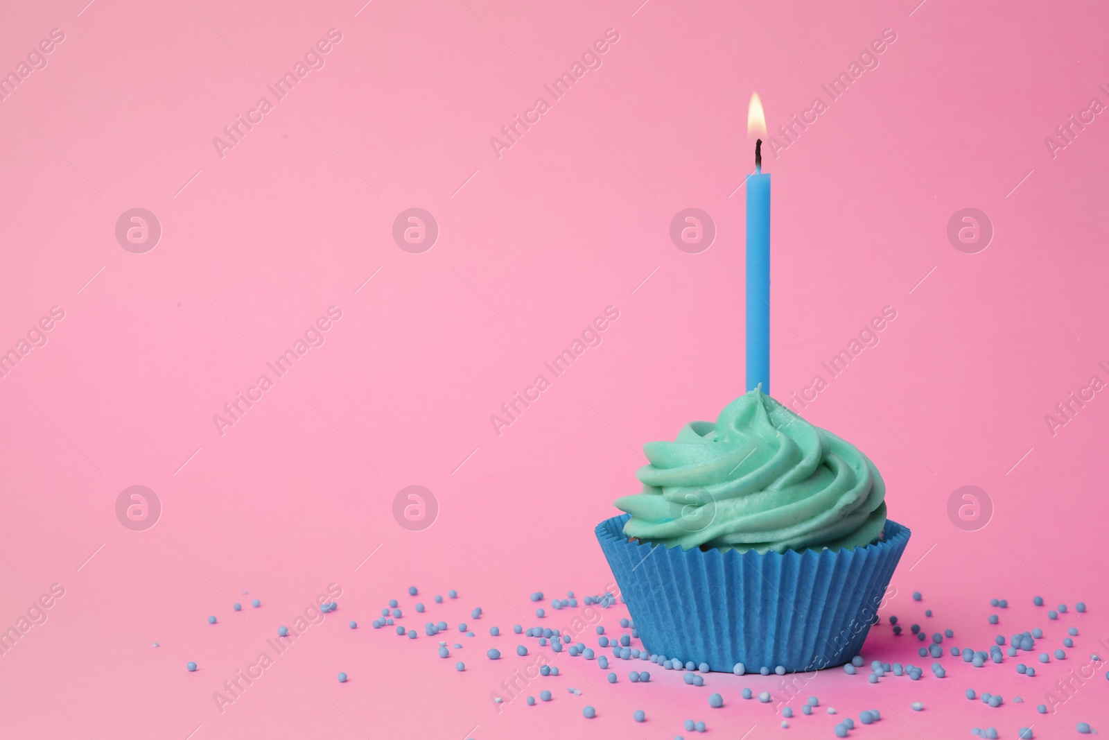 Photo of Delicious birthday cupcake with turquoise cream and burning candle on pink background. Space for text