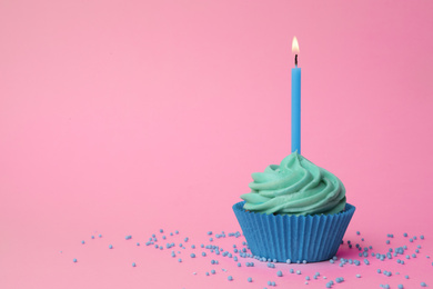 Delicious birthday cupcake with turquoise cream and burning candle on pink background. Space for text