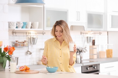 Beautiful young woman having breakfast and drinking milk in kitchen