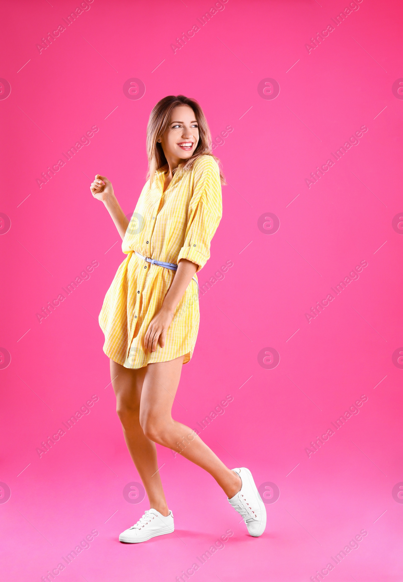 Photo of Beautiful young woman in yellow dress dancing on pink background