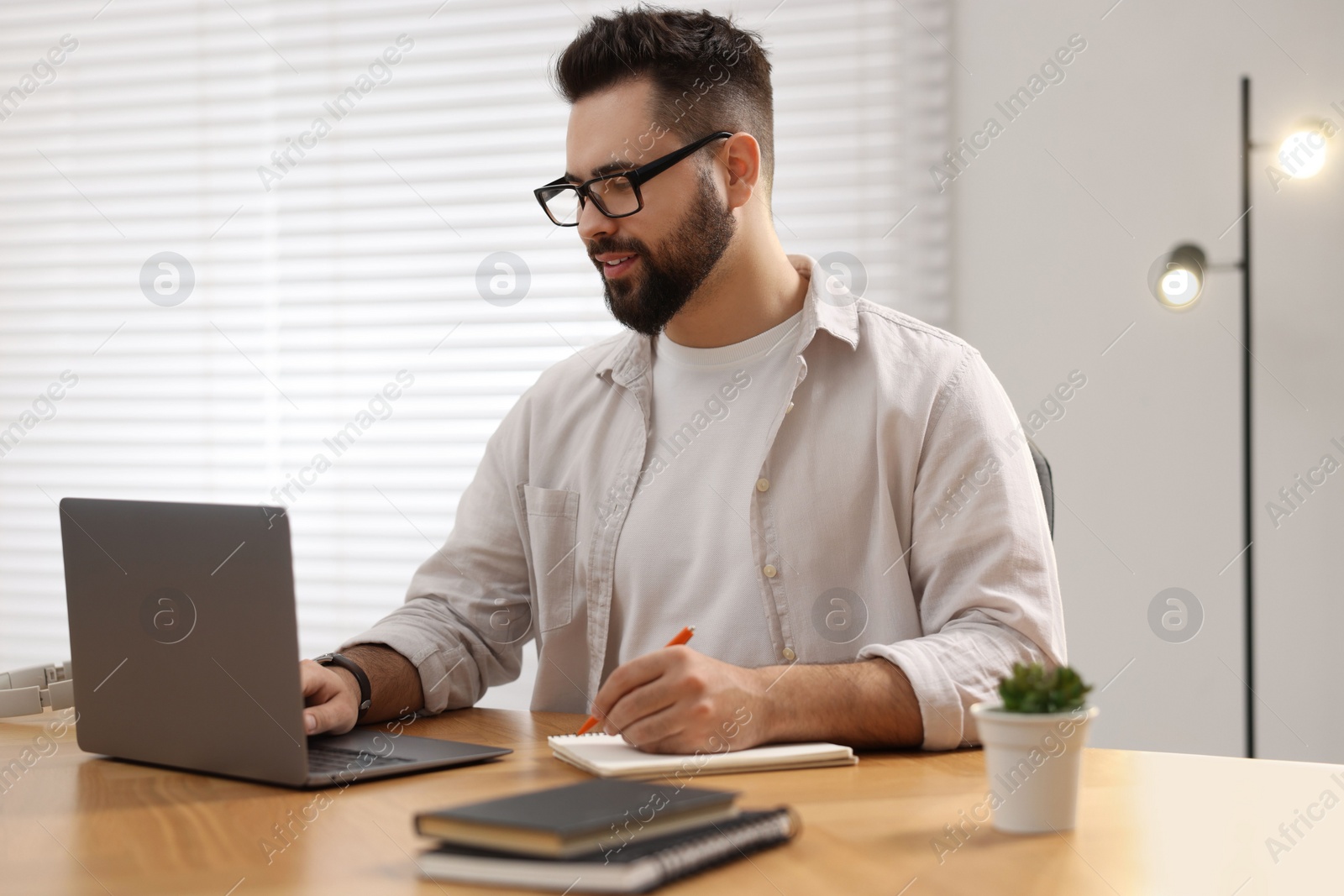 Photo of Young man in glasses watching webinar at table in room