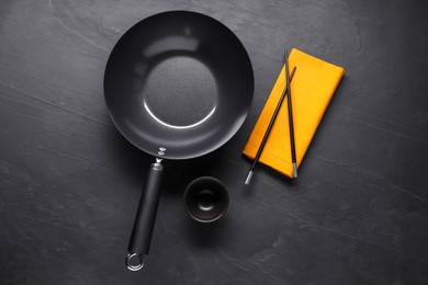 Empty iron wok, sauce bowl and chopsticks on black table, flat lay