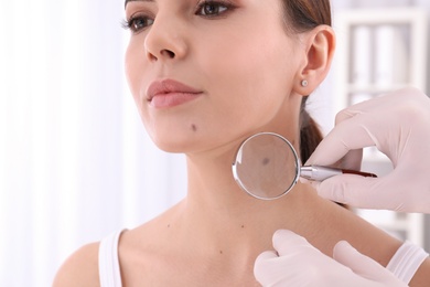 Dermatologist examining patient with magnifying glass in clinic, closeup view