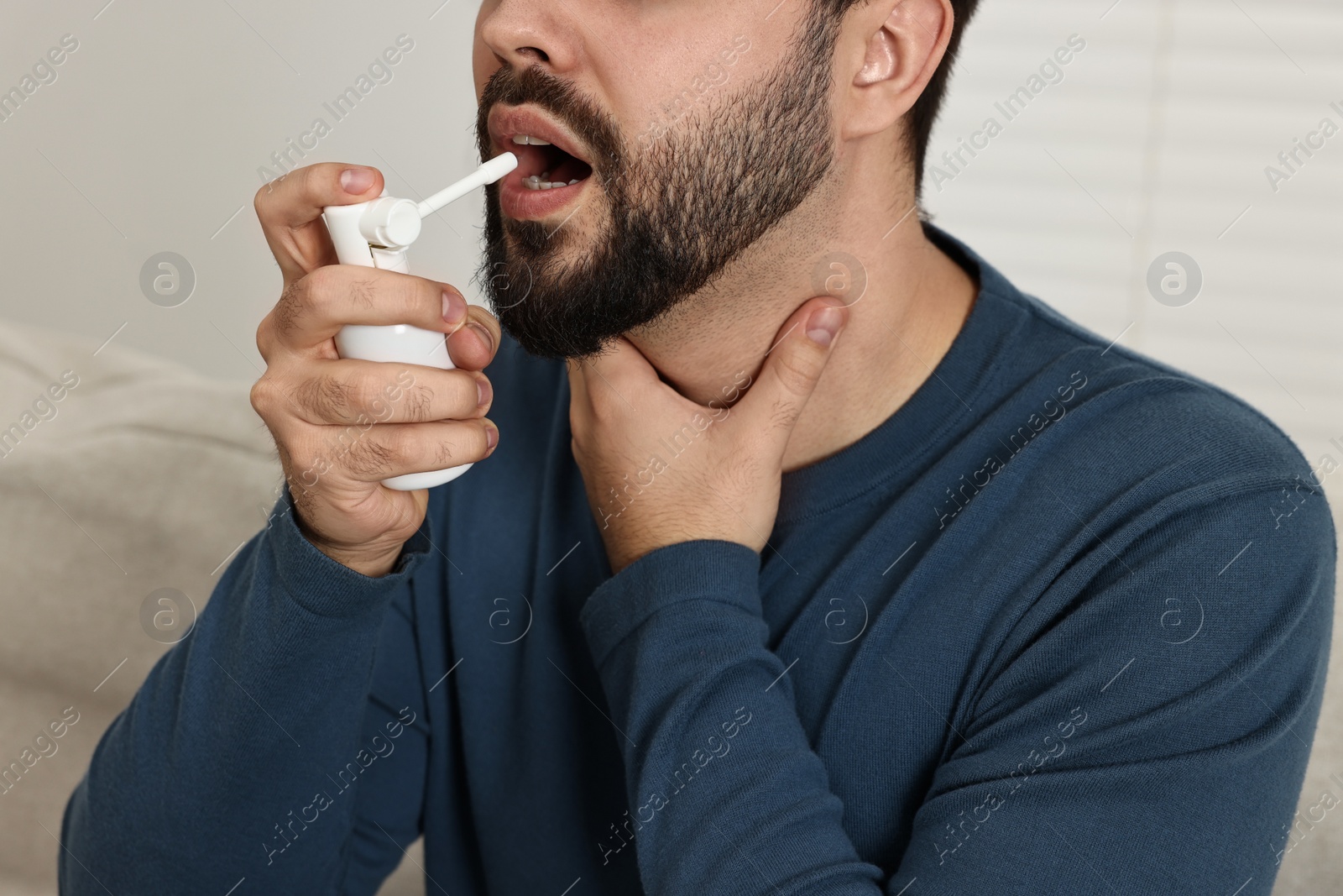 Photo of Young man using throat spray indoors, closeup