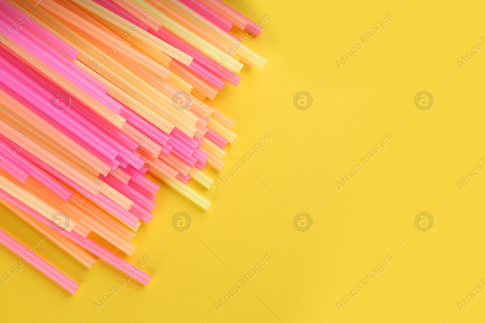 Photo of Heap of colorful plastic drinking straws on yellow background, flat lay. Space for text