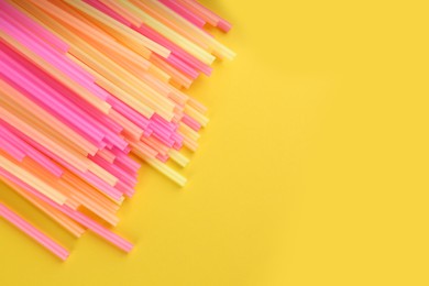 Photo of Heap of colorful plastic drinking straws on yellow background, flat lay. Space for text