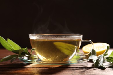 Photo of Cup of aromatic herbal tea and fresh sage on wooden table