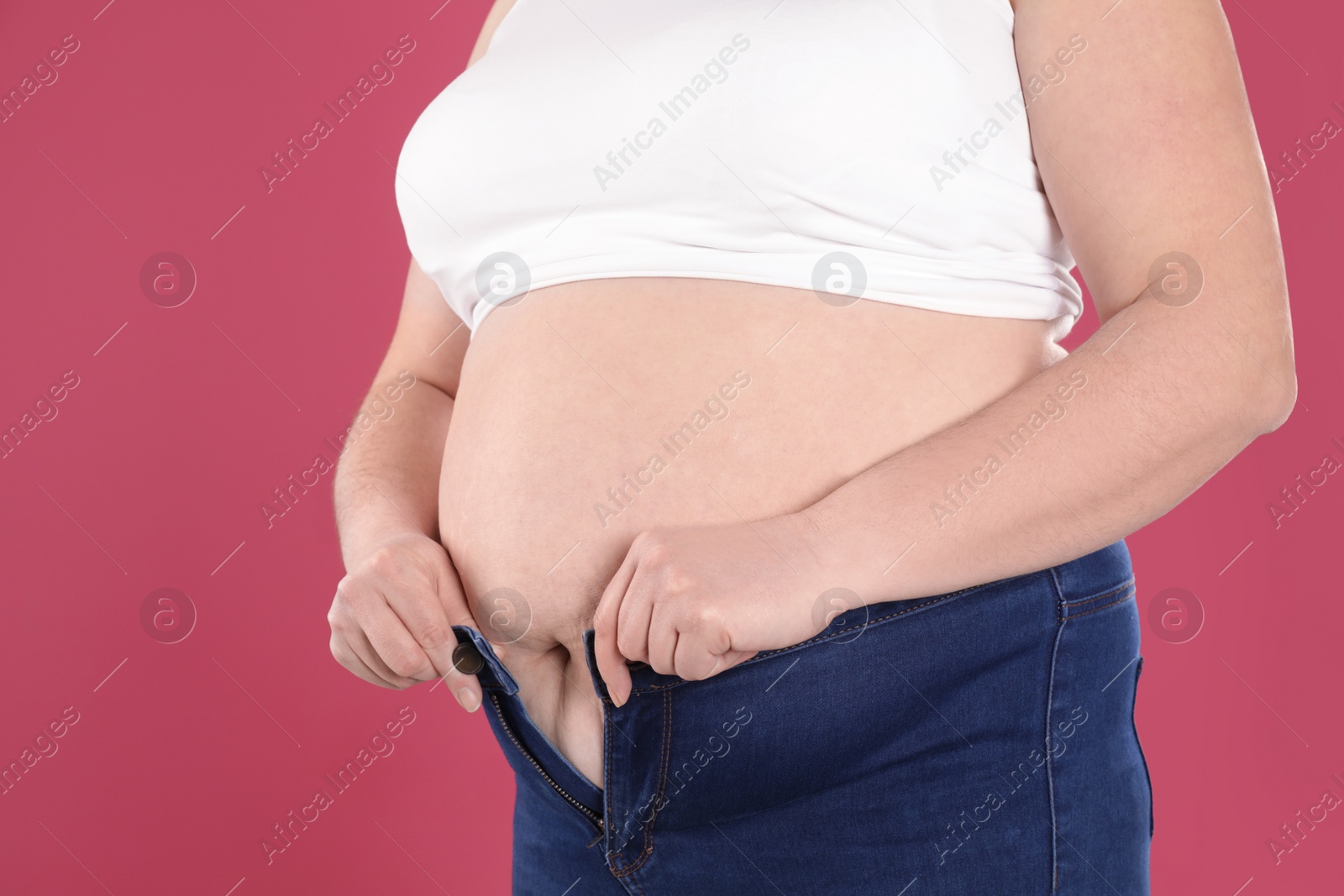 Photo of Overweight woman trying to wear tight jeans on color background, closeup