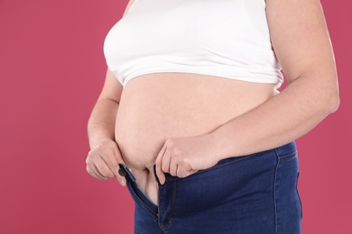 Overweight woman trying to wear tight jeans on color background, closeup