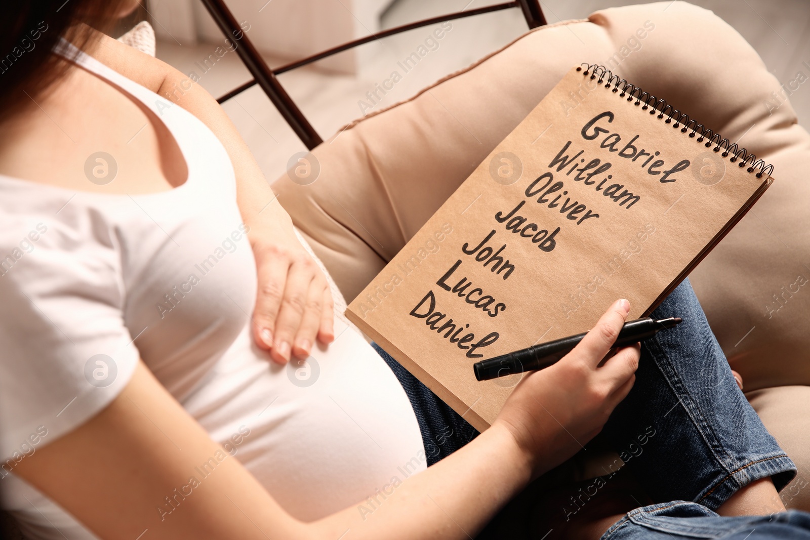 Photo of Pregnant woman with baby names list sitting in armchair, closeup