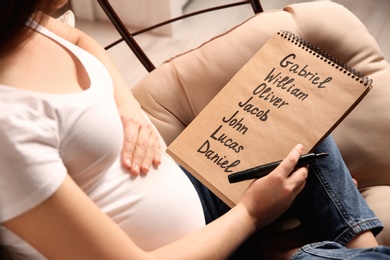 Photo of Pregnant woman with baby names list sitting in armchair, closeup