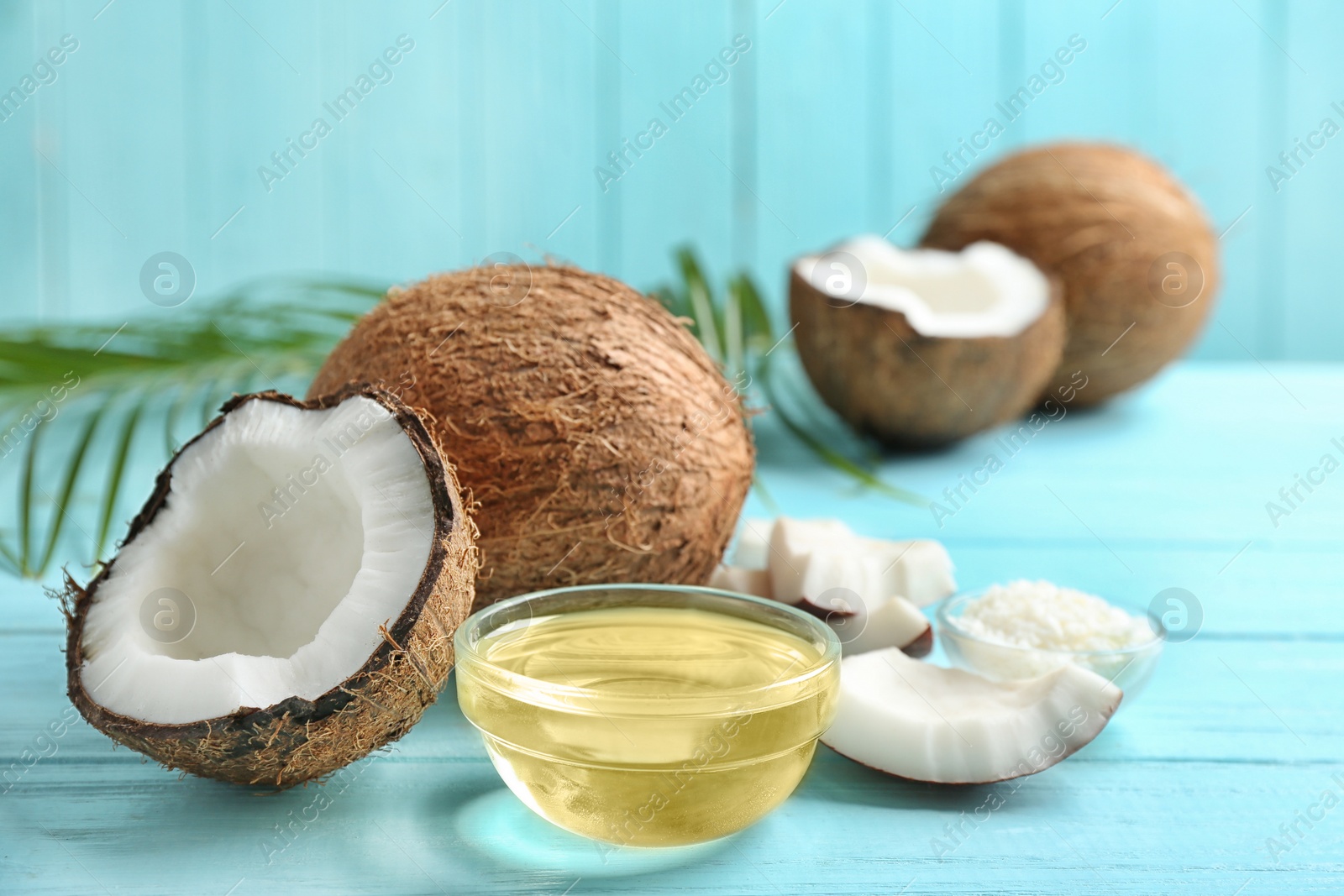 Photo of Bowl of natural organic oil and coconuts on blue wooden table, closeup