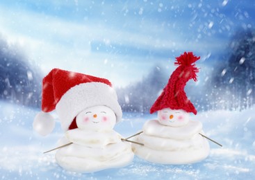 Image of Cute decorative snowmen in red hats outdoors on snowy day