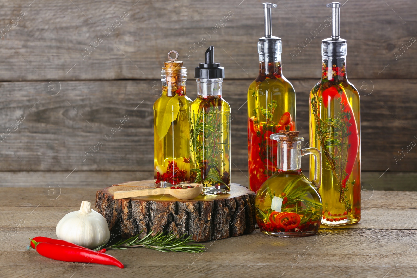 Photo of Cooking oil with different spices and herbs in bottles on wooden table