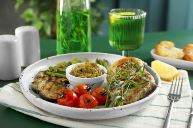 Photo of Tasty chicken, vegetables with tarragon and pesto sauce served on table, closeup