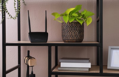 Photo of Modern wi-fi router and houseplant on wooden rack indoors