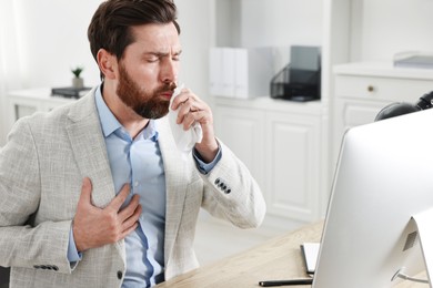 Photo of Sick man with tissue coughing at workplace in office
