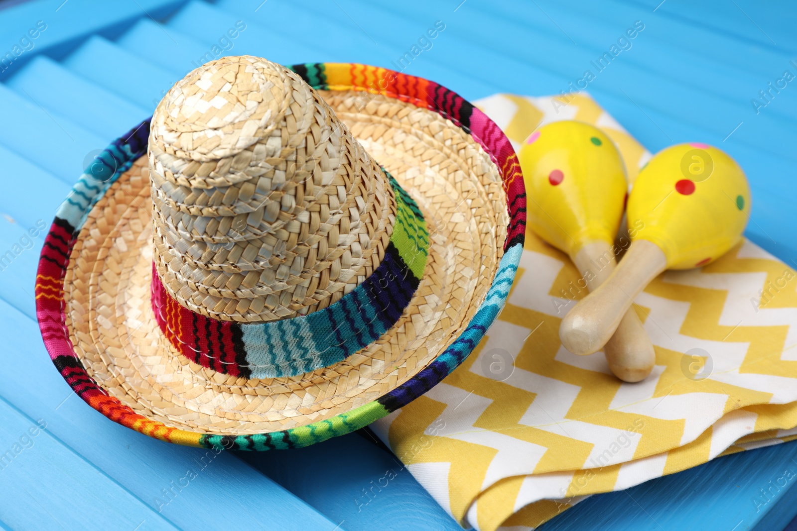 Photo of Mexican sombrero hat, towel and maracas on blue wooden surface