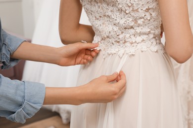 Photo of Woman helping bride wear wedding dress in boutique, closeup