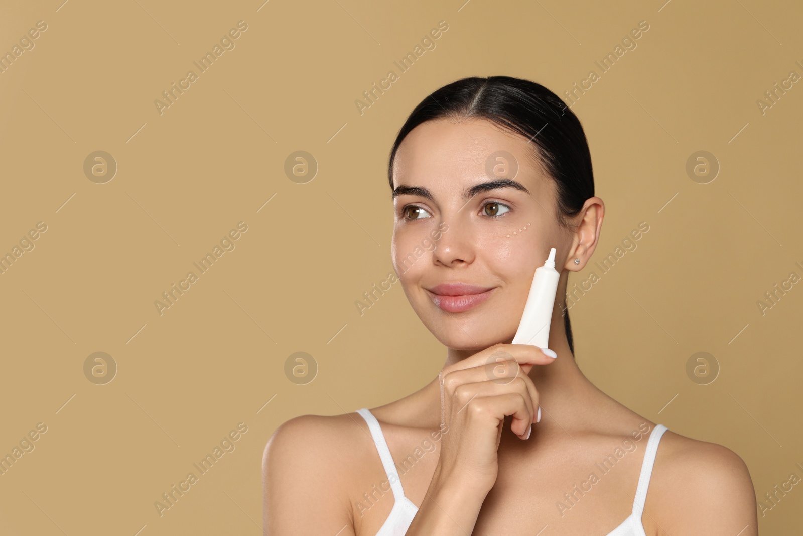 Photo of Beautiful young woman with gel on skin under eye against beige background. Space for text