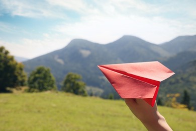 Photo of Woman with red paper plane in mountains on sunny day, closeup. Space for text