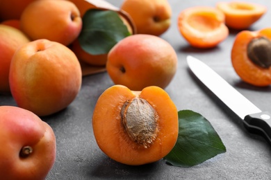 Many fresh ripe apricots and knife on grey table