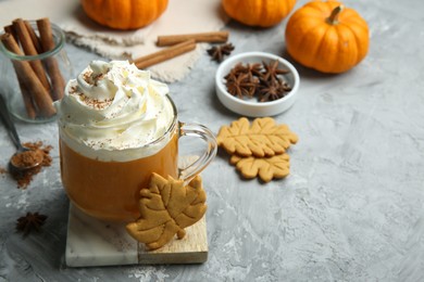 Photo of Cup of pumpkin spice latte with whipped cream, cookies and ingredients on light grey table. Space for text