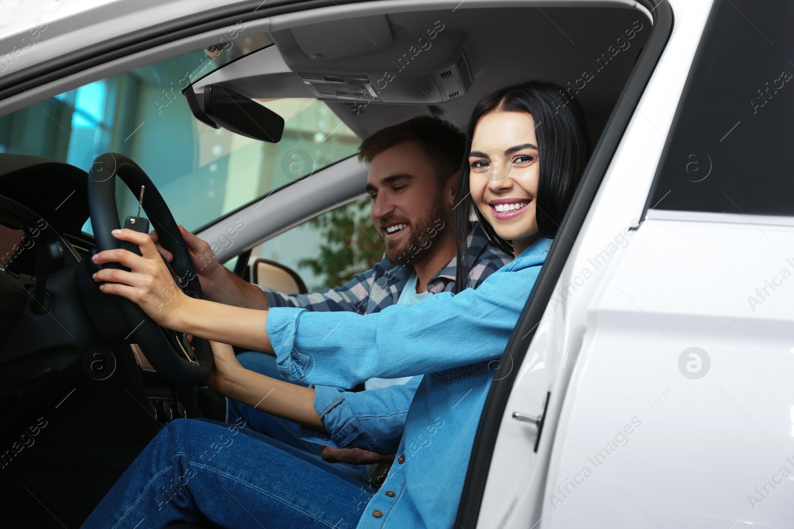 Photo of Happy couple with car key sitting in modern auto at dealership