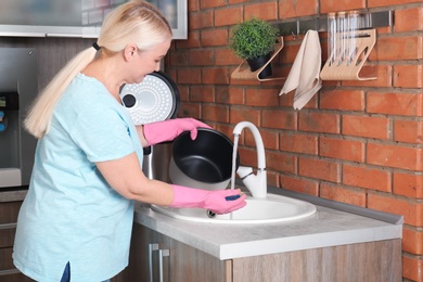 Photo of Mature woman washing modern multi cooker in kitchen sink