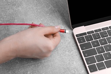 Photo of Woman plugging USB cable with type C connector into laptop port at grey table, closeup