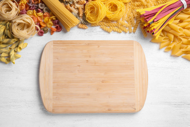 Photo of Different types of pasta and cutting board on white wooden table, flat lay. Space for text