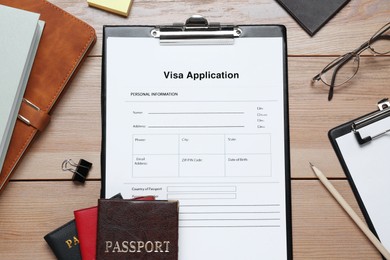 Photo of Visa application form for immigration, passports and stationery on wooden table, flat lay