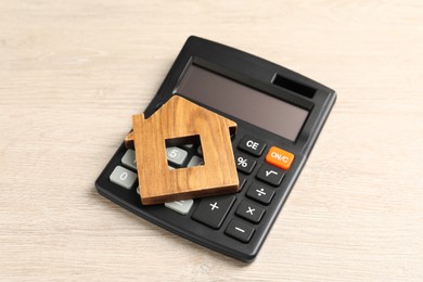 Mortgage concept. House model and calculator on wooden table, closeup