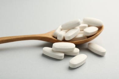 Photo of Vitamin pills and wooden spoon on light grey background, closeup. Health supplement