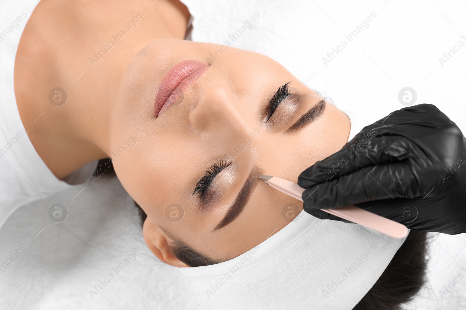 Photo of Young woman having professional eyebrow correction procedure in beauty salon