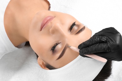 Photo of Young woman having professional eyebrow correction procedure in beauty salon