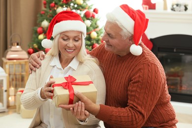 Photo of Happy mature man presenting Christmas gift to his wife at home