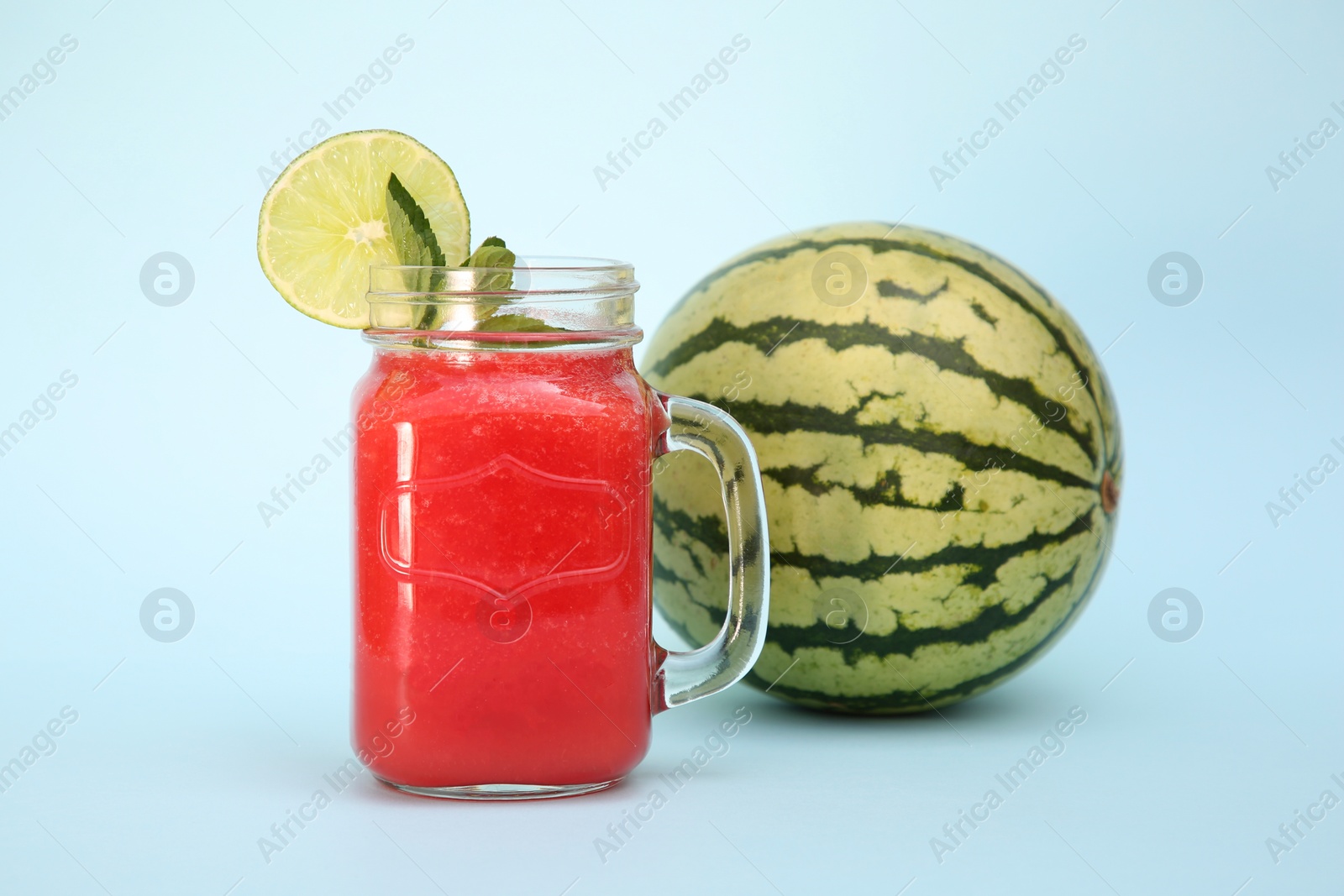 Photo of Glass of delicious drink with mint, lime and fresh watermelon on light blue background