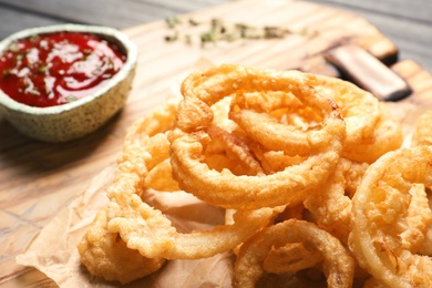 Photo of Homemade crunchy fried onion rings and sauce on cutting board, closeup