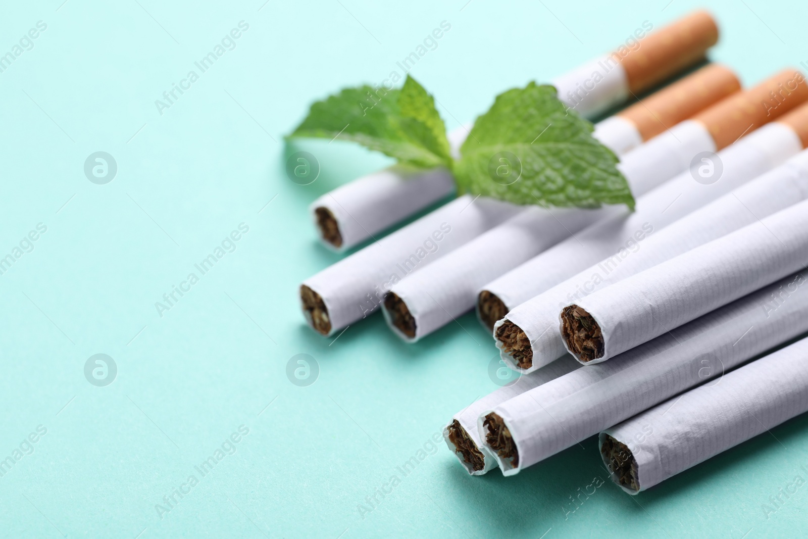 Photo of Menthol cigarettes and mint on turquoise background, closeup. Space for text