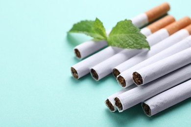 Photo of Menthol cigarettes and mint on turquoise background, closeup. Space for text