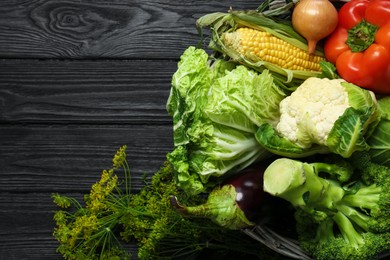 Different fresh vegetables in wicker basket on black wooden table, top view and space for text. Farmer harvesting