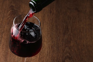 Photo of Pouring tasty red wine in glass at wooden table, closeup. Space for text