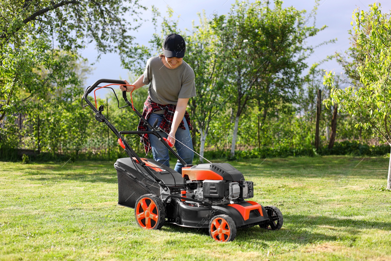 Photo of Smiling woman cutting green grass with lawn mower in garden