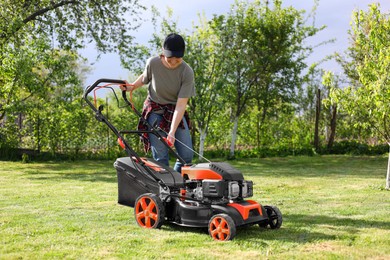 Smiling woman cutting green grass with lawn mower in garden